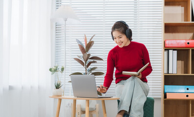 Embracing the Online World: A woman in her living space, focused on her laptop and wearing...
