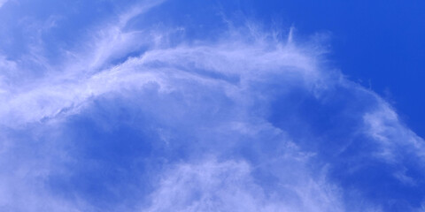 Thin, wispy clouds stretch across a deep blue sky, creating a soft and airy visual perfect for a...