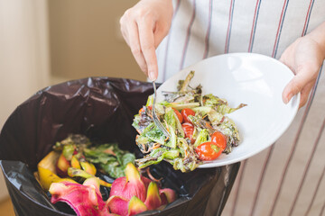 Compost from leftover food housekeeper woman, female hand holding salad dish or plate use fork scraping waste, rotten vegetable throwing away into garbage, trash or bin. Environmentally responsible.