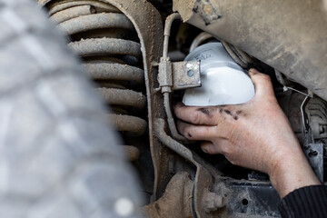 Mechanic's hand reaches out to install or remove an oil filter on the underbody of a car. Changing an oil filter