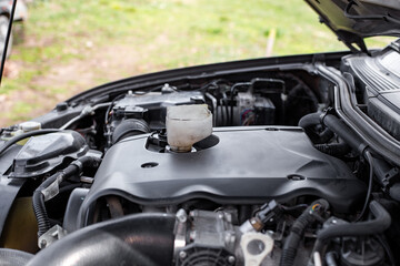 Car engine with hood open, funnel inserted to pour engine oil into engine oil filler neck