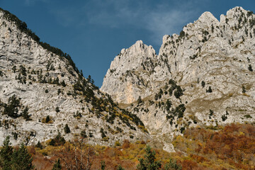 Sharp ridges and colorful forested slopes of the Prokletije mountains in autumn, captured in warm...