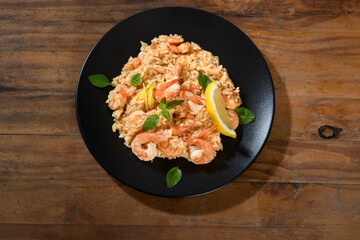 Shrimp risotto with lemon and basil on a black plate on a wooden table