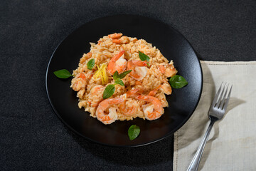 Shrimp risotto on a black plate with fresh herbs on a black background