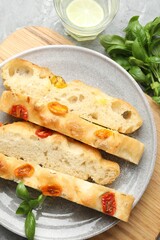 Pieces of delicious focaccia with tomatoes, basil and glass of water on gray textured table, flat lay