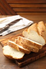 Cut bread loaf, spikelets and knife on wooden table, closeup