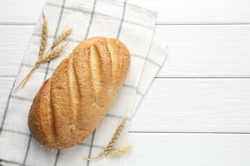 Fresh bread loaf and spikelets on white wooden table, flat lay. Space for text