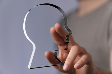 Abstract image of a person's hand interacting with a transparent head outline, symbolizing...