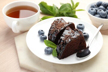 Pieces of delicious bundt cake with blueberries, mint, chocolate shavings and tea on wooden table, closeup