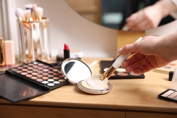 Woman with brush and eyeshadow palette at wooden vanity indoors, closeup