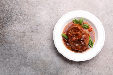 Traditional ossobuco dish with beef steak and sauce on grey table, top view. Space for text