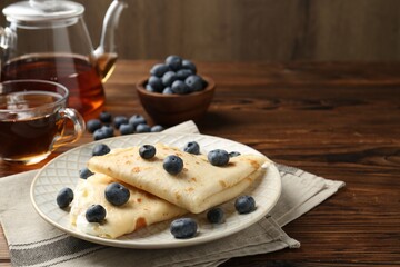Tasty crepes with cream, blueberries and tea on wooden table, closeup
