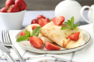Tasty crepes with cream, strawberries and mint served on table, closeup