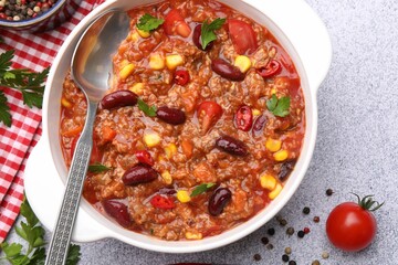 Tasty chili con carne in bowl and ingredients on grey table, flat lay