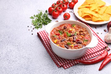 Tasty chili con carne in bowl, nachos and ingredients on grey table, closeup. Space for text