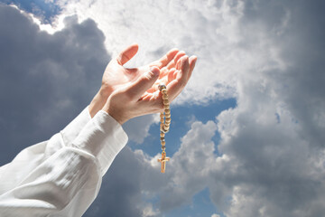 Praying hands with wooden rosary with cross against the sky. Concept of Christianity