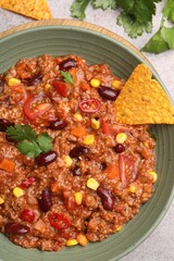 Tasty chili con carne in bowl and nachos on grey table, flat lay