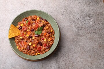 Tasty chili con carne in bowl and nachos on grey table, top view. Space for text