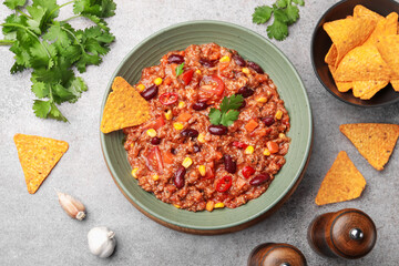 Tasty chili con carne in bowl and nachos on grey table, flat lay