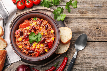 Tasty chili con carne in bowl, ingredients and bread on wooden table, flat lay. Space for text