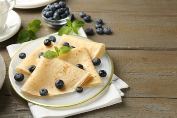 Tasty crepes with blueberries and mint on wooden table. Space for text