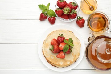 Delicious crepes with strawberries, honey, mint and tea on white wooden table, flat lay. Space for text