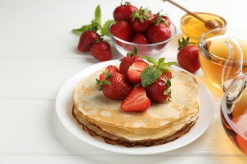 Delicious crepes with strawberries, honey, mint and tea on white wooden table, closeup