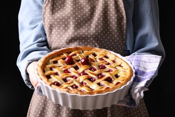 Woman holding tasty cherry pie on black background, closeup