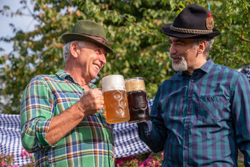 Senior men with beer mugs with Bavarian beer in Tyrolean hats celebrating a beer festival in Germany. Happy old people during the October holiday in Munich