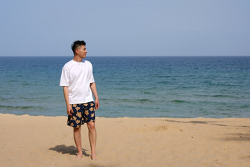Asian man standing on a sandy beach, looking at blue ocean and sky in Sanya, Hainan, China