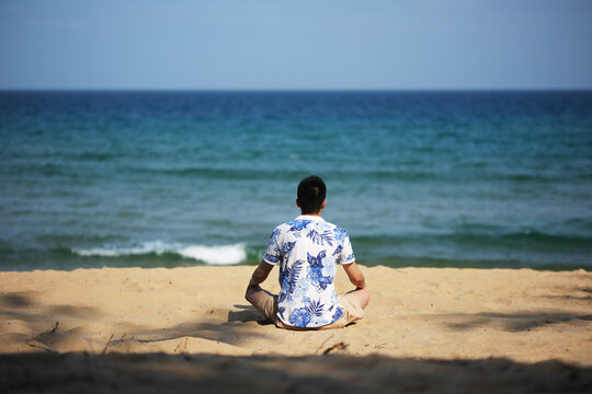 Man sitting on the beach facing the sea, rear view. In Sanya, Hainan, China - Powered by Adobe