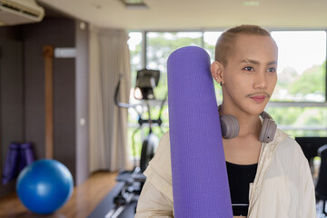 Non-binary gay man with mustache and androgynous appearance working out indoors in gym. Wearing feminine sports bra and using water bottle. Inclusive fitness concept with genderfluid representation.