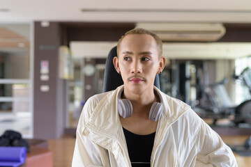 Obraz premium Non-binary gay man with mustache and androgynous appearance working out indoors in gym. Wearing feminine sports bra and using water bottle. Inclusive fitness concept with genderfluid representation.