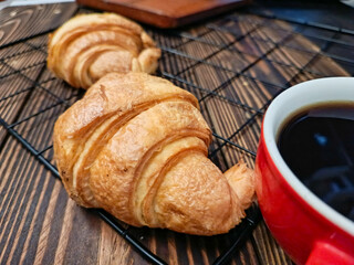 Three croissants on a cooling rack beside a red cup of black coffee.