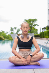 Genderfluid individual with mustache and lipstick relaxing poolside while wearing a bikini-style...