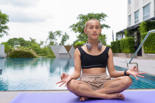 Genderfluid individual with mustache and lipstick relaxing poolside while wearing a bikini-style top. Confident, expressive LGBTQ+ representation in summer lifestyle setting.