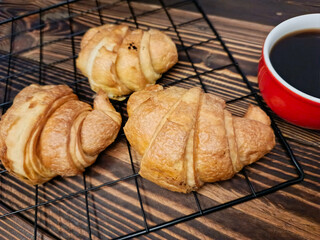 Three croissants on a cooling rack beside a red cup of black coffee.