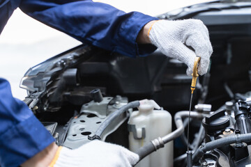 Close-up shot mechanician checking engine lubricant oil level at auto service station.