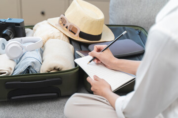 person checking list of stuff to prepare suitcase before travel