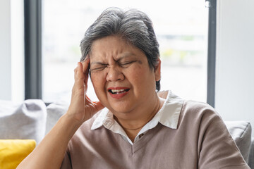Elderly women feeling dizzy and headache sit on the sofa at home.