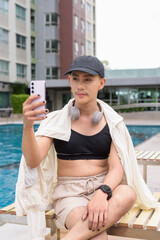 Genderfluid gay man with mustache and lipstick relaxing poolside while wearing a bikini-style top....