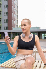 Genderfluid individual with mustache and lipstick relaxing poolside while wearing a bikini-style...