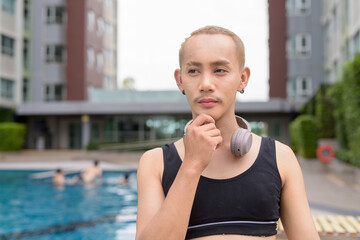Genderfluid gay man with mustache and lipstick relaxing poolside while wearing a bikini-style top....