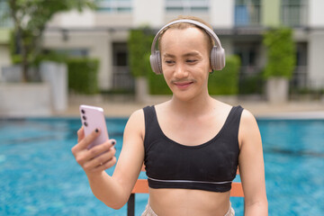 Genderfluid individual with mustache and lipstick relaxing poolside while wearing a bikini-style...
