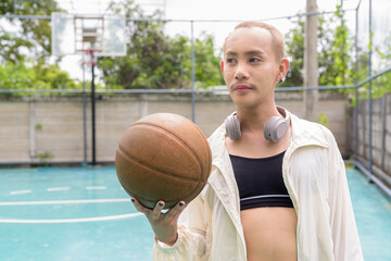 Nonbinary androgynous individual wearing sportswear posing on outdoor basketball court. Confident, athletic expression of LGBTQ+ identity and physical self-empowerment.