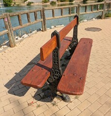 Banco de parque de madera con dos asientos y patas de hierro fundido, al lado de un estanque con cerca de madera 