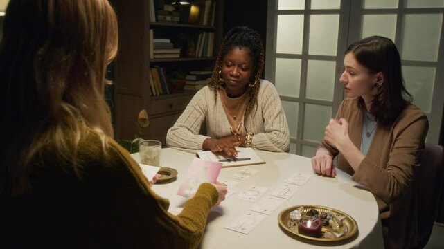 Two biracial best friends asking fortune teller to do tarot reading. They giving her photo of young African American man