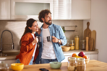 Two individuals share a joyful moment in a welcoming home office kitchen, holding coffee mugs and appreciating each other’s company during a peaceful morning.