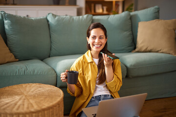 Woman sitting on a couch with a coffee cup in hand, engaging in a voice call using her smartphone...