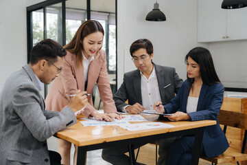 Team Discussion in Office: Four business professionals in smart attire gather around a wooden...